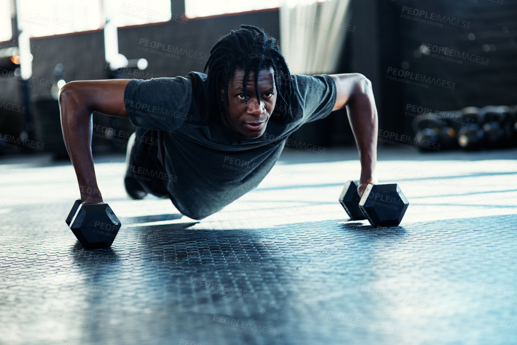 Buy stock photo Shot of a young man doing push ups with dumbbells in a gym