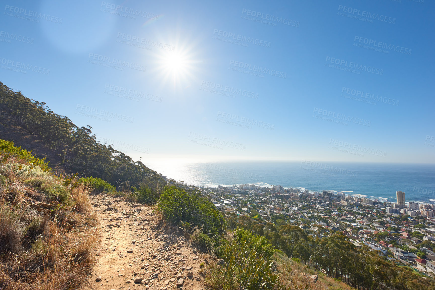 Buy stock photo Mountainous hiking trail high above a coastal city in South Africa against a blue horizon. Remote walking path on table mountain on a sunny day with sun flare. Popular tourist location in Cape Town