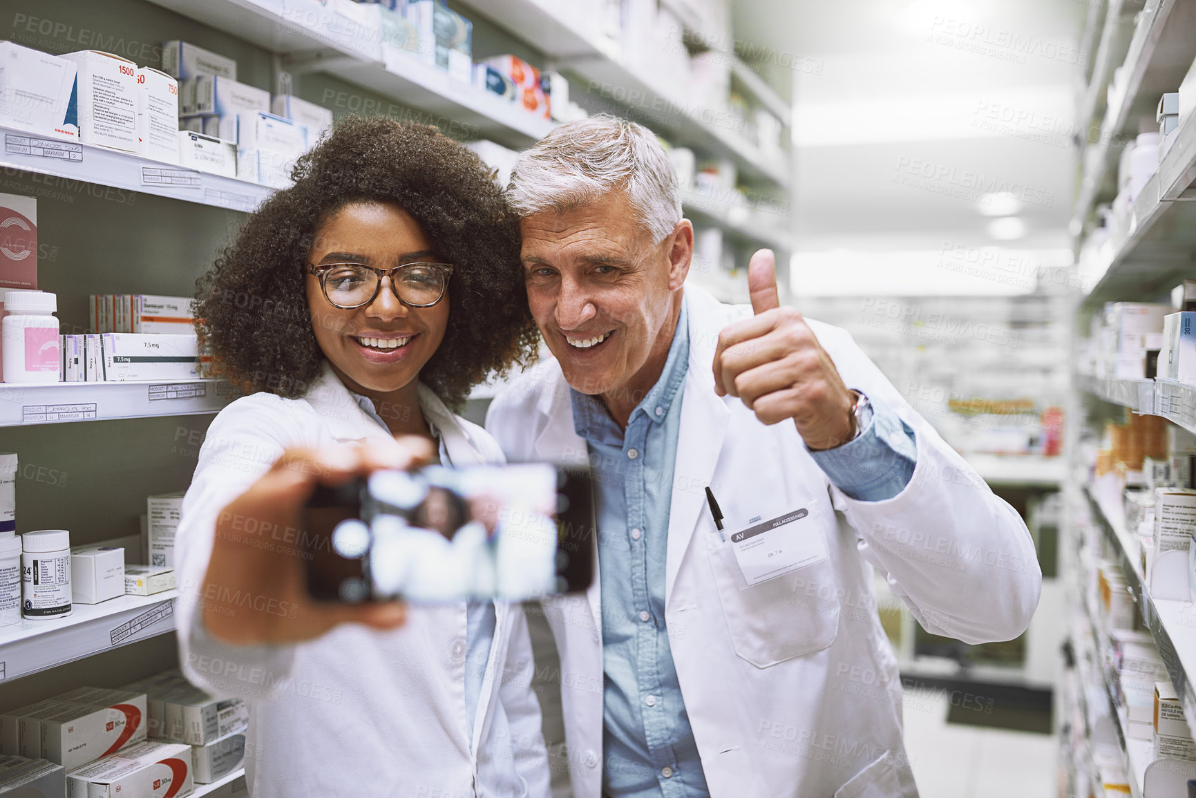 Buy stock photo Shot of two cheerful pharmacists posing together for a self portrait while one shows thumbs up