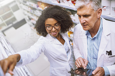 Buy stock photo High angle shot of two focused pharmacist walking around and doing stock inside of a pharmacy