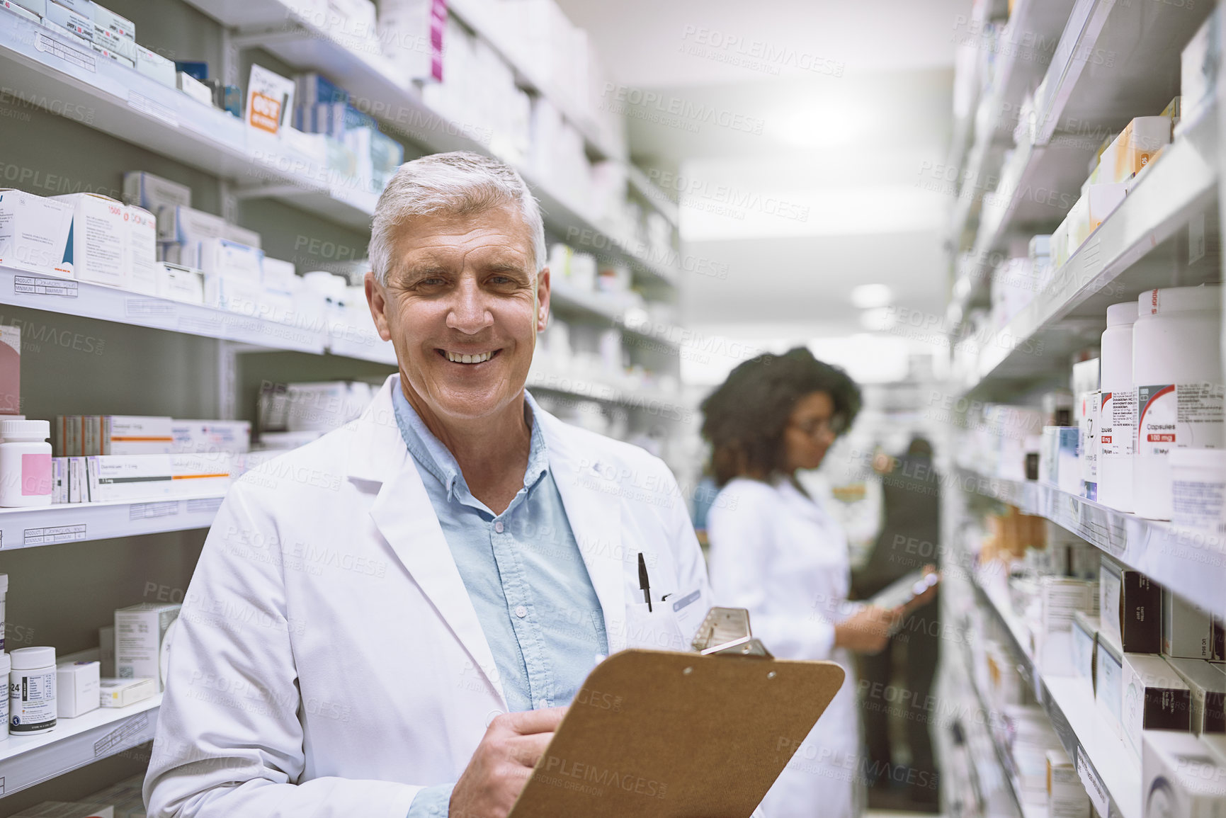 Buy stock photo Portrait of a cheerful mature male pharmacist holding a clipboard and doing stock while looking at the camera in a pharmacy
