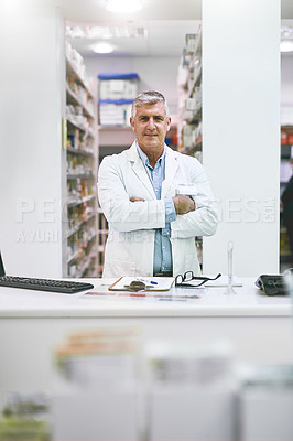Buy stock photo Portrait of a cheerful mature male pharmacist standing with arms folded while looking at the camera in a pharmacy