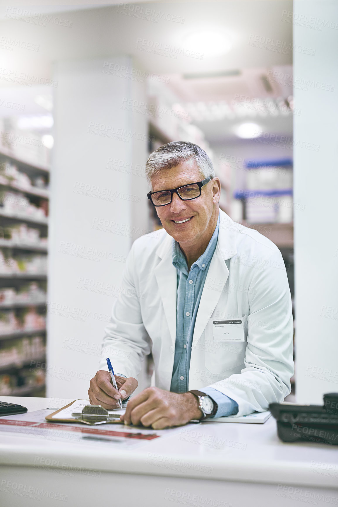 Buy stock photo Portrait of a confident mature male pharmacist making notes in a book on the counter while looking at the camera
