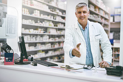 Buy stock photo Portrait of a cheerful mature male pharmacist reaching out to give a handshake while looking at the camera