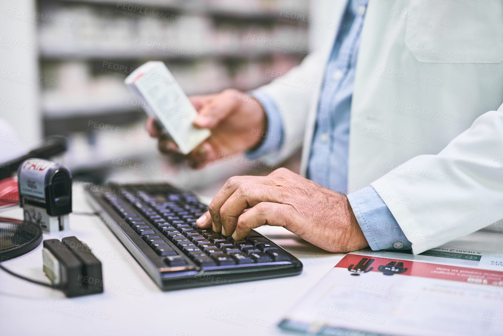 Buy stock photo Shot of a unrecognizable pharmacist typing on a computer keyboard while holding a medication subscription