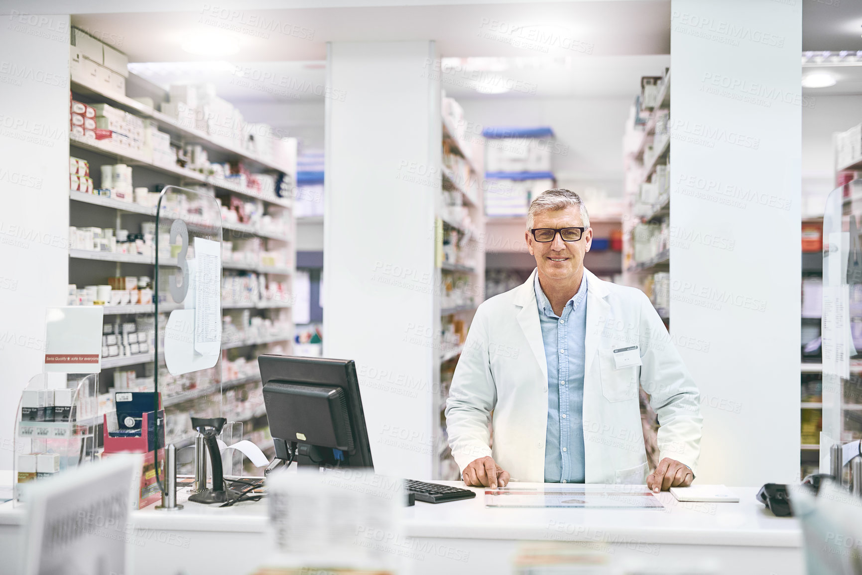 Buy stock photo Portrait of a cheerful mature male pharmacist standing behind the counter while looking at the camera in a pharmacy