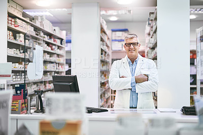Buy stock photo Portrait of a cheerful mature male pharmacist standing with his arms folded while looking at the camera in a pharmacy