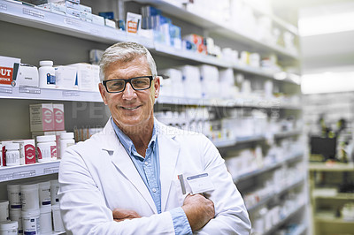 Buy stock photo Portrait of a cheerful mature male pharmacist standing with his arms folded while looking at the camera in a pharmacy
