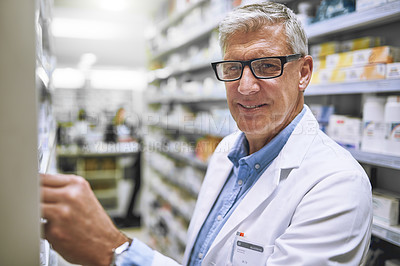 Buy stock photo Portrait of a cheerful mature male pharmacist getting medication from a shelf while looking at the camera in a pharmacy