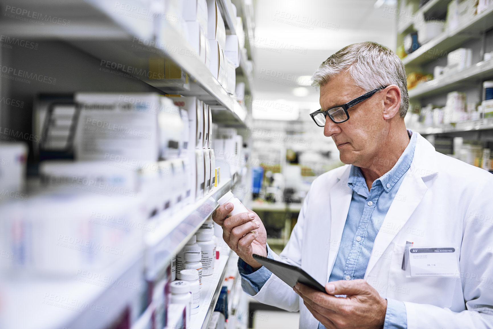 Buy stock photo Shot of a focused mature male pharmacist holding a medication box and reading it in a pharmacy