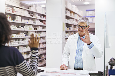 Buy stock photo Shot of a cheerful mature male pharmacist greeting a customer inside of the pharmacy