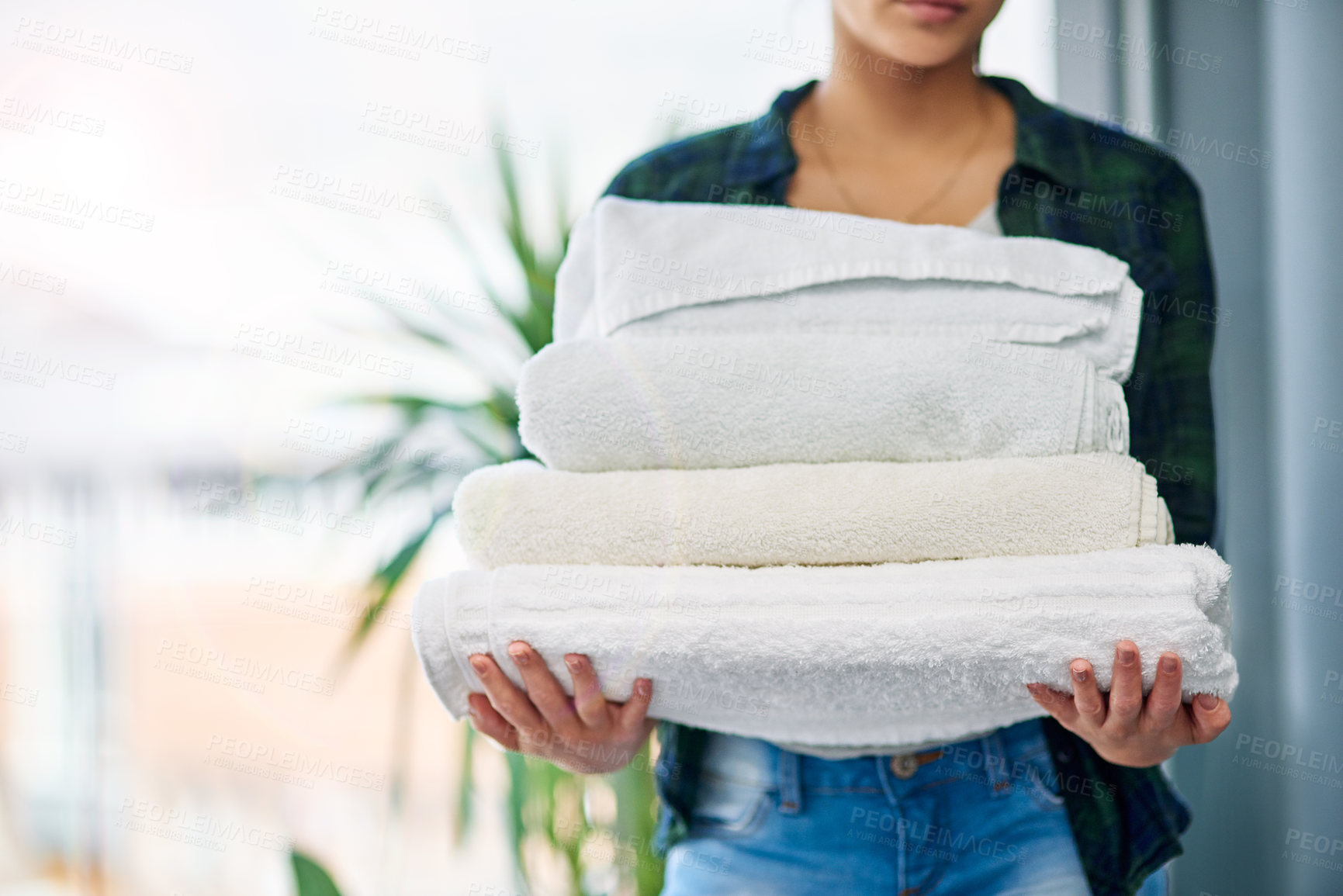 Buy stock photo Cropped shot of an unrecognizable woman carrying a pile of towels while doing laundry at home