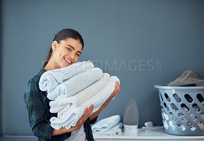 Buy stock photo Cropped portrait of an attractive young woman carrying a pile of towels while doing laundry at home