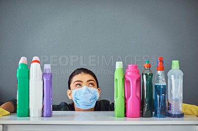 Buy stock photo Studio shot of an attractive young woman wearing a mask while surrounded by cleaning products