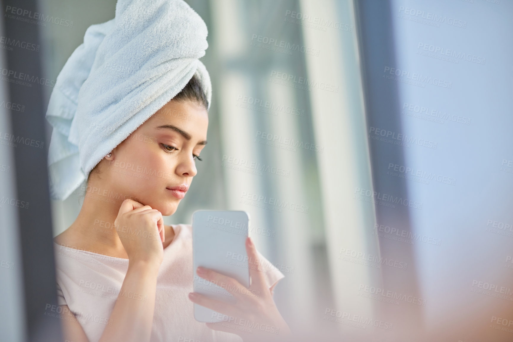 Buy stock photo Cropped shot of a beautiful young woman using her cellphone to check her skin in the bathroom at home