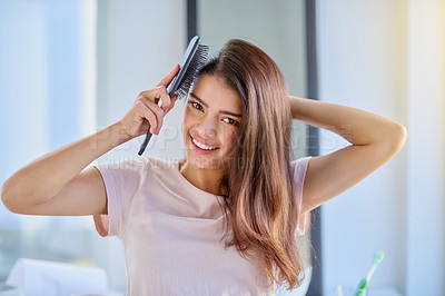 Buy stock photo Cropped portrait of a beautiful young woman brushing her hair in the bathroom at home