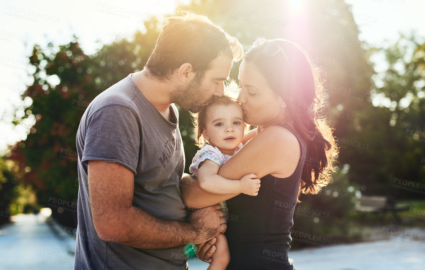 Buy stock photo Happy, kiss and parents with baby in park for bonding, loving relationship and relax together outdoors. Family, sunshine and mother, father and child for embrace, affection and love on weekend