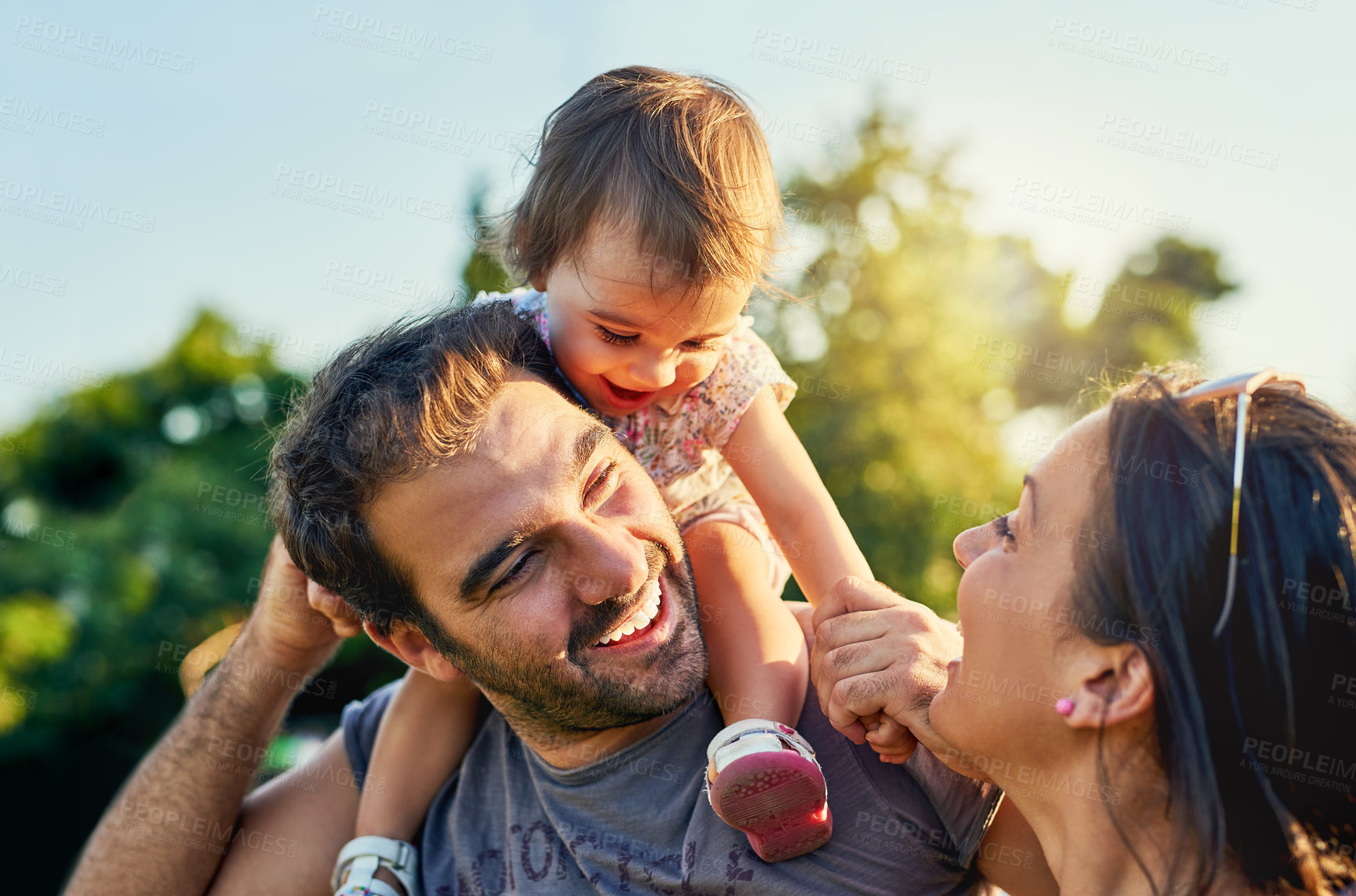 Buy stock photo Family, father and daughter on shoulders in park with happy mom, love and summer sunshine. Young couple, baby girl or laugh together for freedom, bond and helping hand for care, backyard or garden