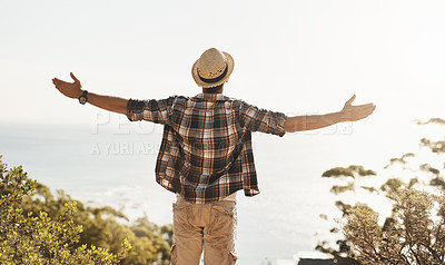 Buy stock photo Rearview shot of an unrecognizable young man standing with his arms outstretched while hiking in the mountains