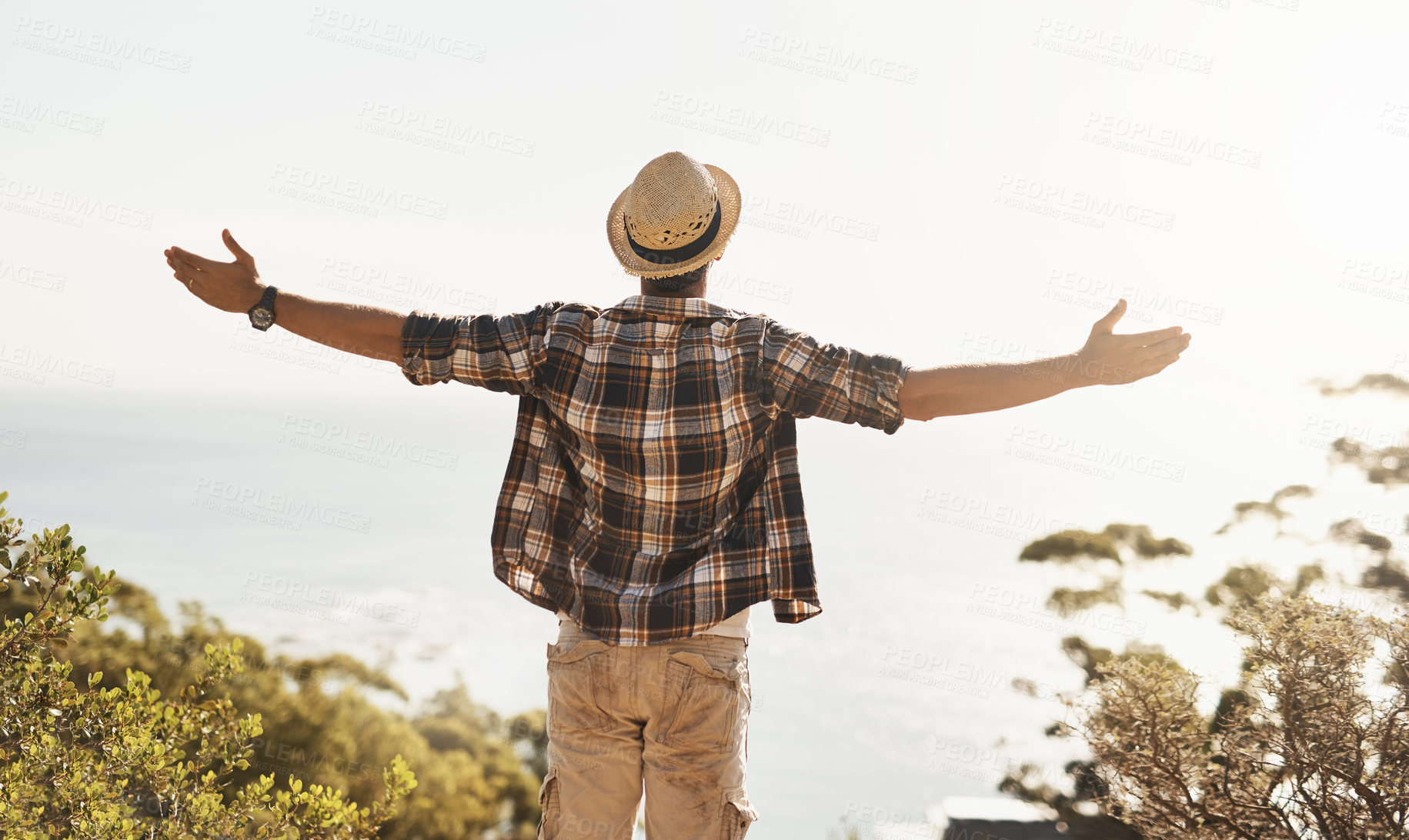 Buy stock photo Rearview shot of an unrecognizable young man standing with his arms outstretched while hiking in the mountains