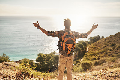 Buy stock photo Rearview shot of an unrecognizable young man standing with his arms outstretched while hiking in the mountains