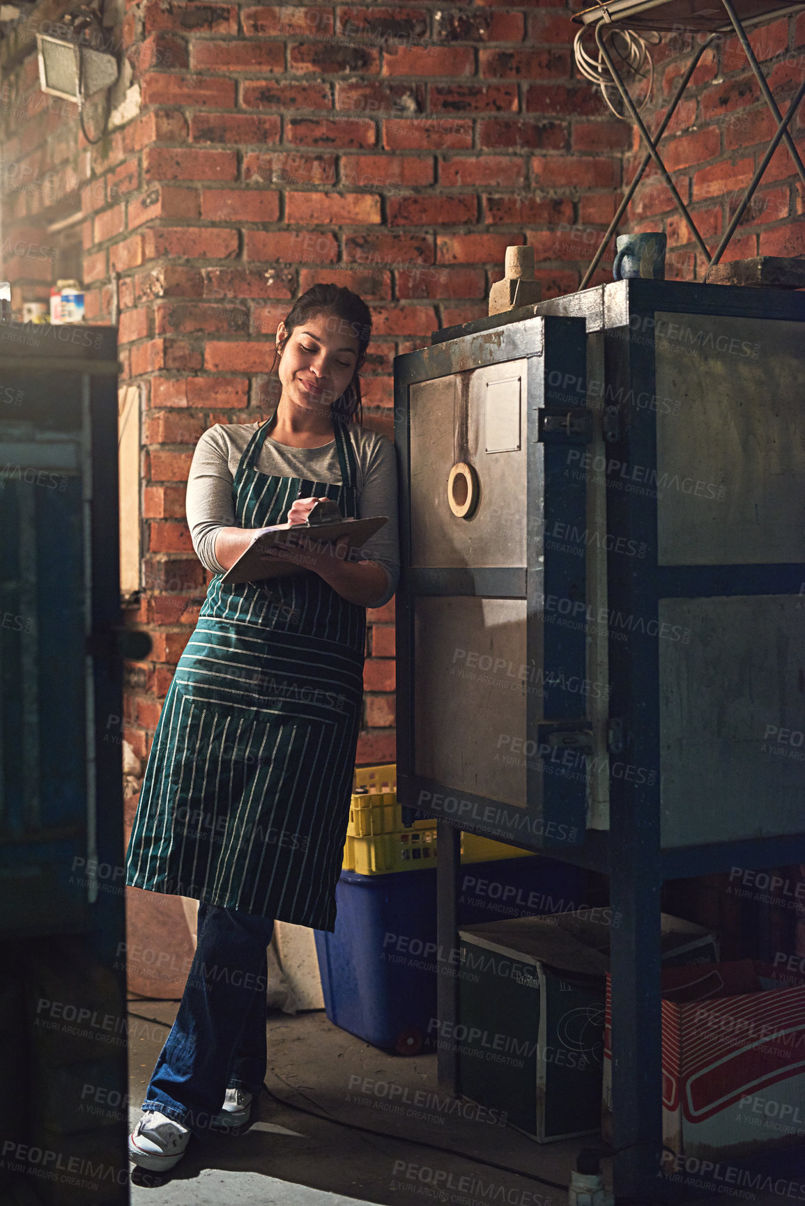 Buy stock photo Shot of a young entrepreneur writing on a clipboard in a workshop