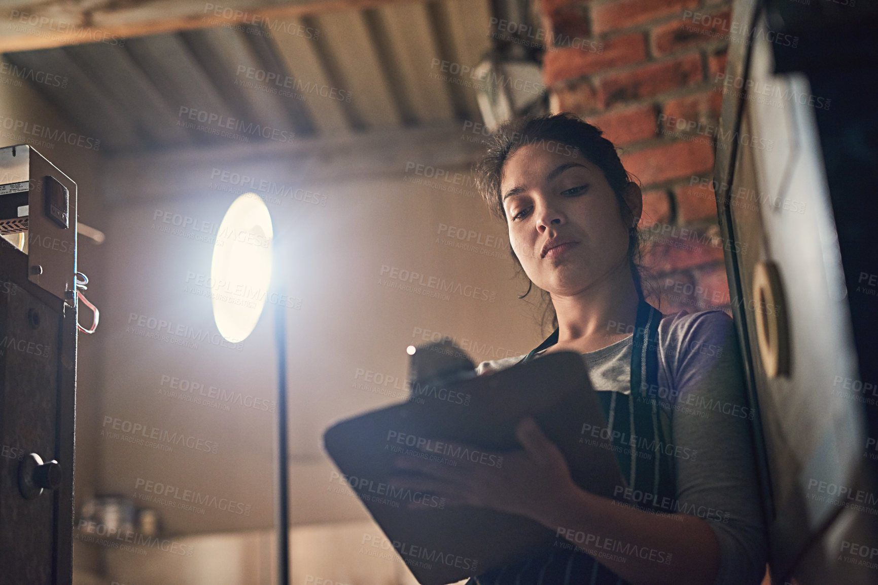 Buy stock photo Shot of a young entrepreneur writing on a clipboard in a workshop