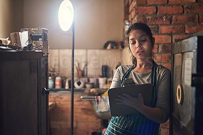 Buy stock photo Shot of a young entrepreneur writing on a clipboard in a workshop