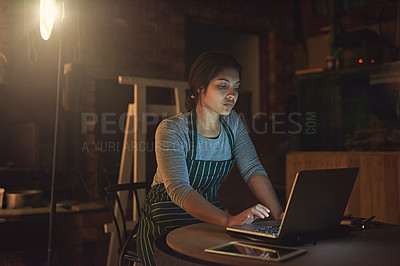 Buy stock photo Shot of a young entrepreneur working late on a laptop in a workshop