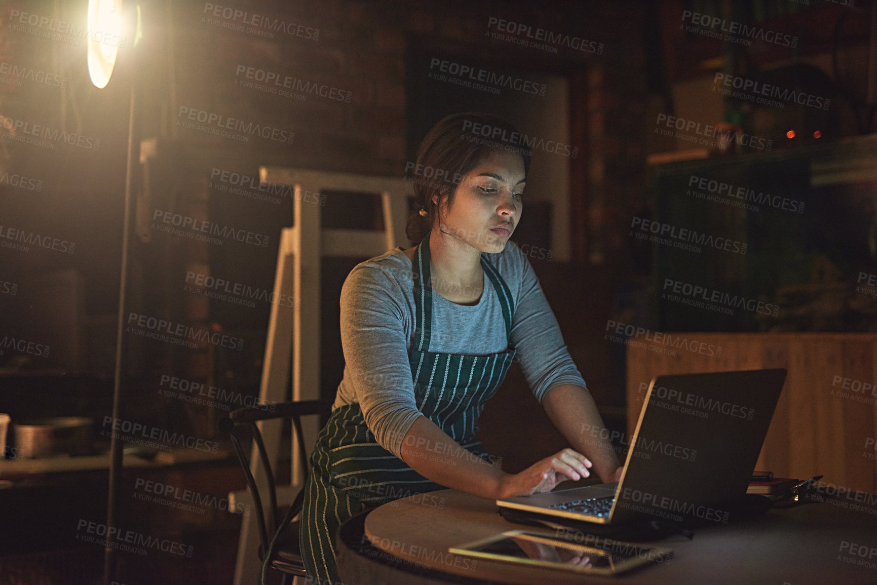 Buy stock photo Shot of a young entrepreneur working late on a laptop in a workshop