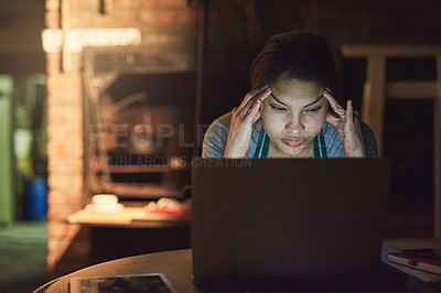 Buy stock photo Shot of a young entrepreneur looking stressed out while working late on a laptop in a workshop