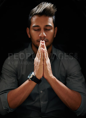 Buy stock photo Shot of a focused young man standing with his hands together and praying with his eyes closed