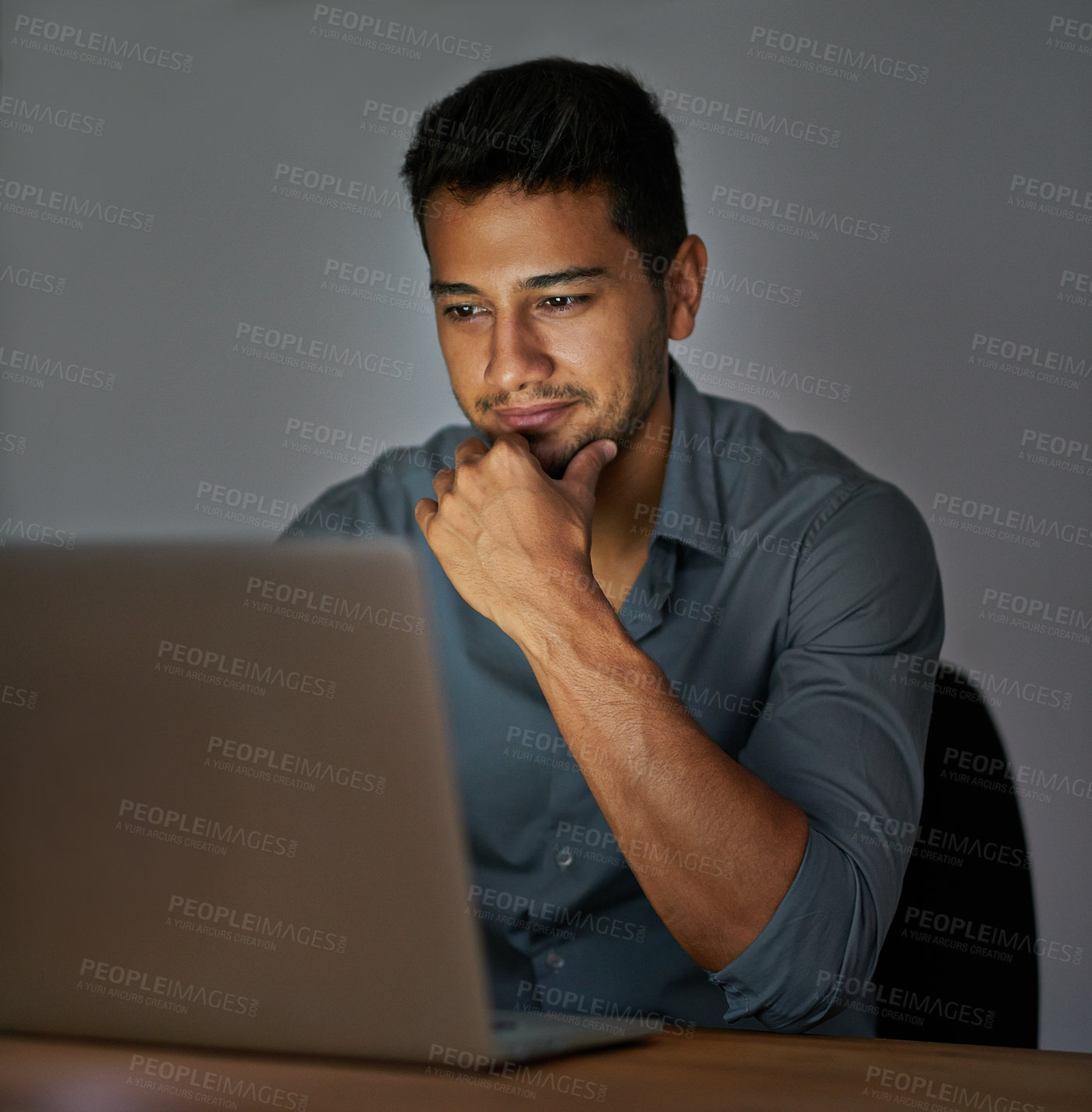 Buy stock photo Shot of a confident young man working on a laptop in the office at night