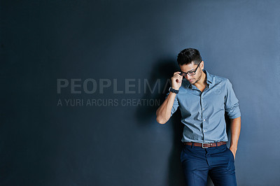 Buy stock photo Studio shot of a focused young man wearing glasses while standing with one hand in his pocket and looking down