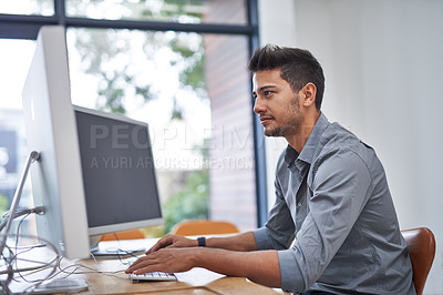 Buy stock photo Shot of a confident young man working on his computer in the office during the day