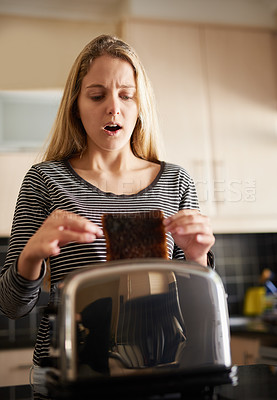 Buy stock photo Shot of a young woman removing a slice of burnt toast from a toaster at home