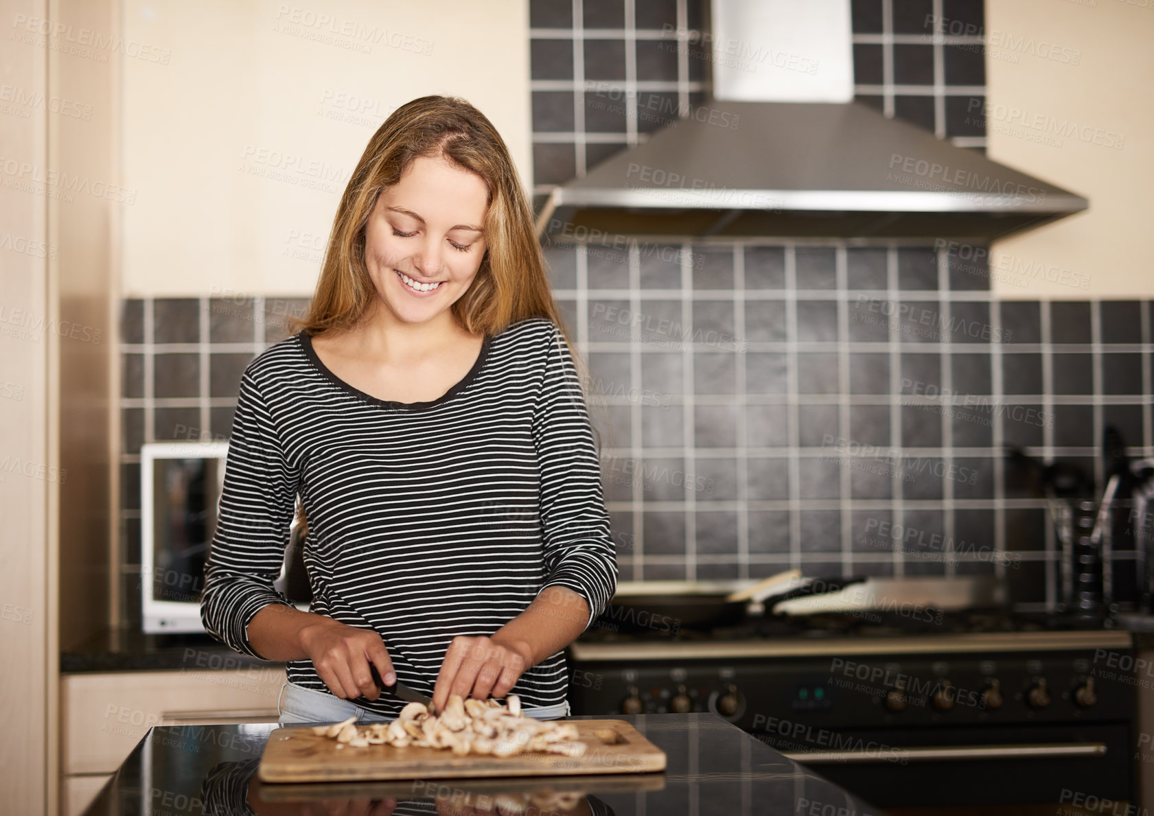 Buy stock photo Shot of a happy young woman slicing mushrooms on a chopping board in the kitchen