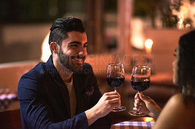 Buy stock photo Shot of a cheerful young couple  having a celebratory toast with wine glasses while looking into each other's eyes over dinner outside at night