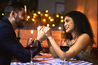 Buy stock photo Shot of a cheerful young couple holding hands while looking into each other's eyes over a candle lit dinner date at night