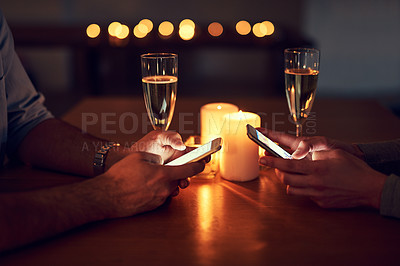 Buy stock photo Cropped shot of a unrecognizable couple texting on their mobile phones over a candle lit dinner at night