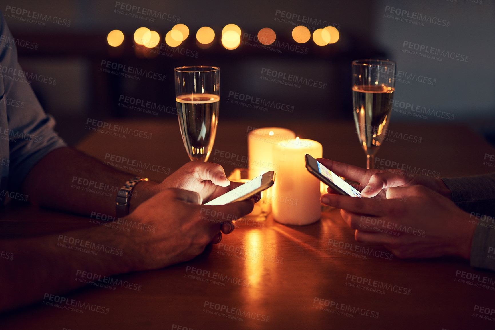 Buy stock photo Cropped shot of a unrecognizable couple texting on their mobile phones over a candle lit dinner at night