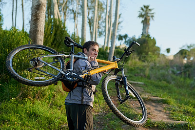 Buy stock photo Rearview shot of a handsome male athlete carrying his bike while mountain biking through the forest