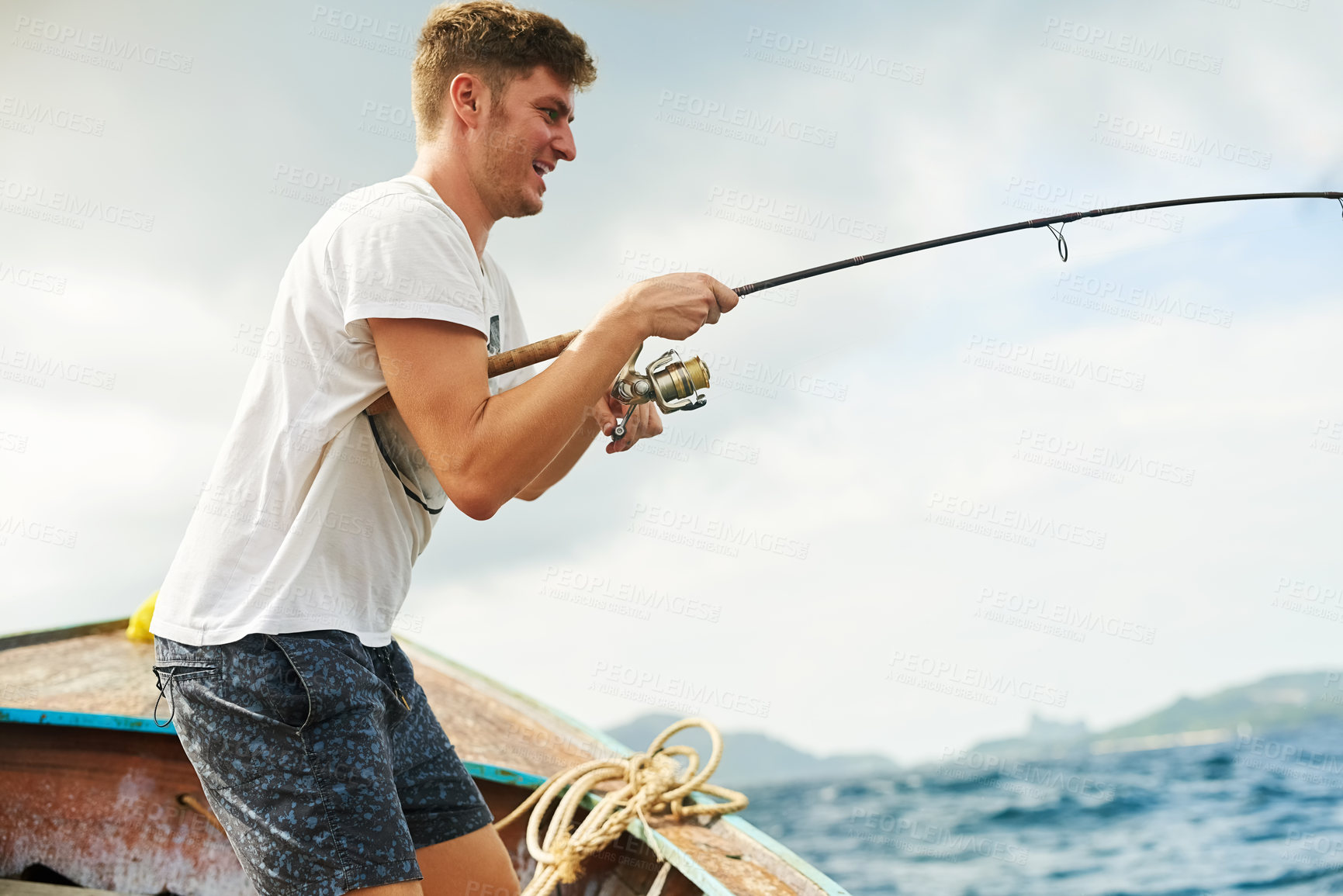 Buy stock photo Cropped shot of a handsome young man fishing while out at sea on his boat