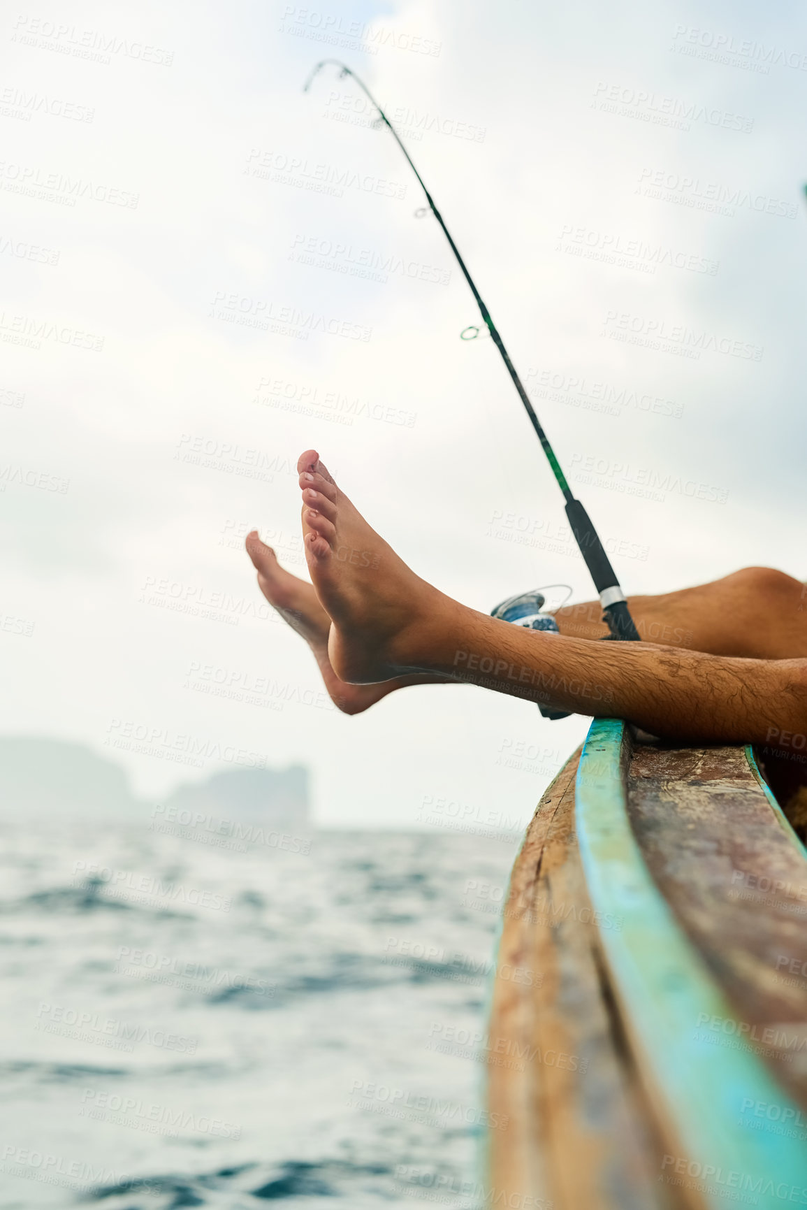 Buy stock photo Cropped shot of an unrecognizable young man fishing while out at sea on his boat