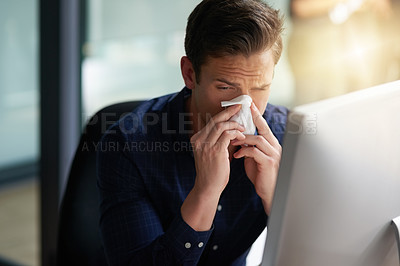 Buy stock photo Shot of a young businessman blowing his nose in an office