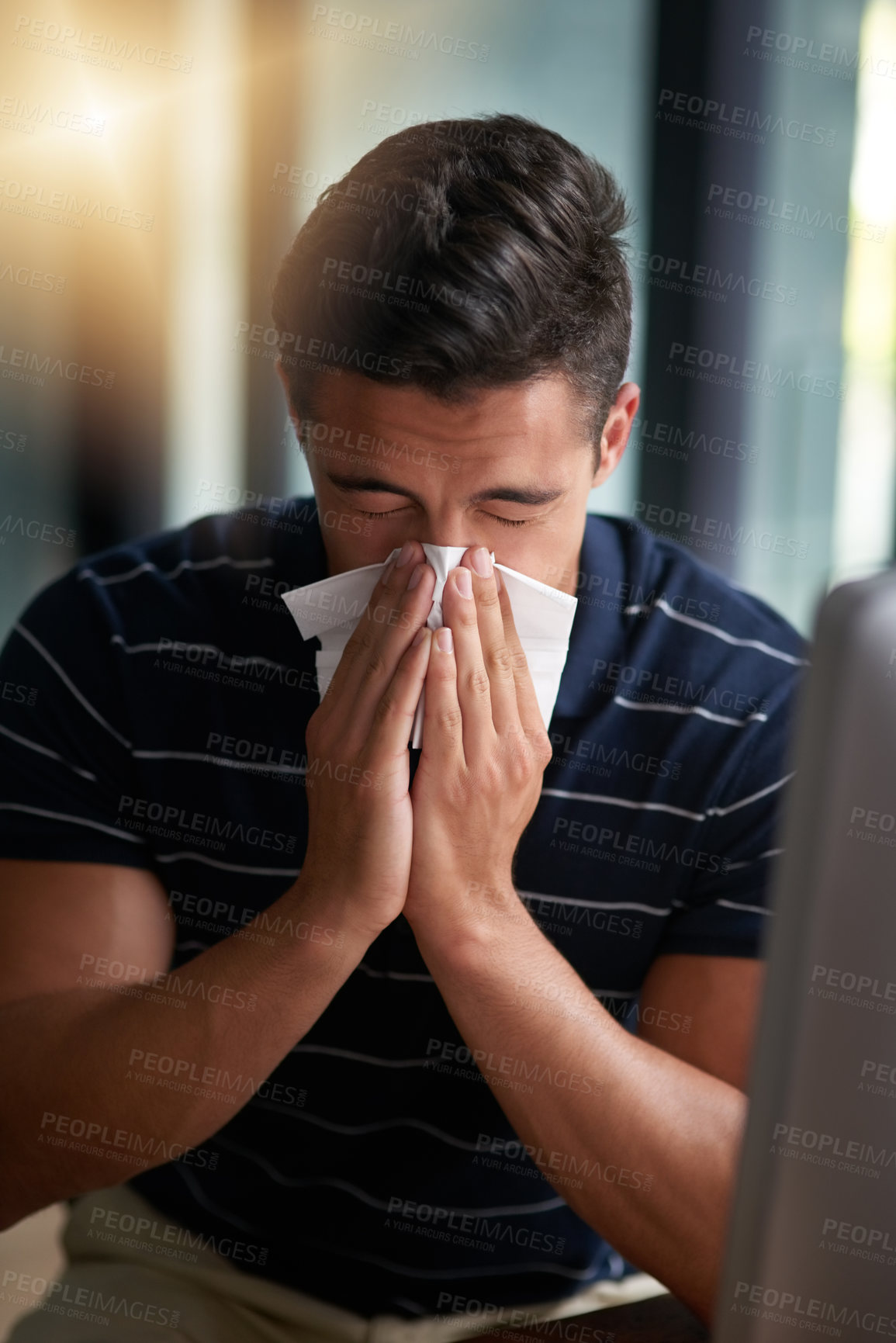 Buy stock photo Shot of a young businessman blowing his nose in an office