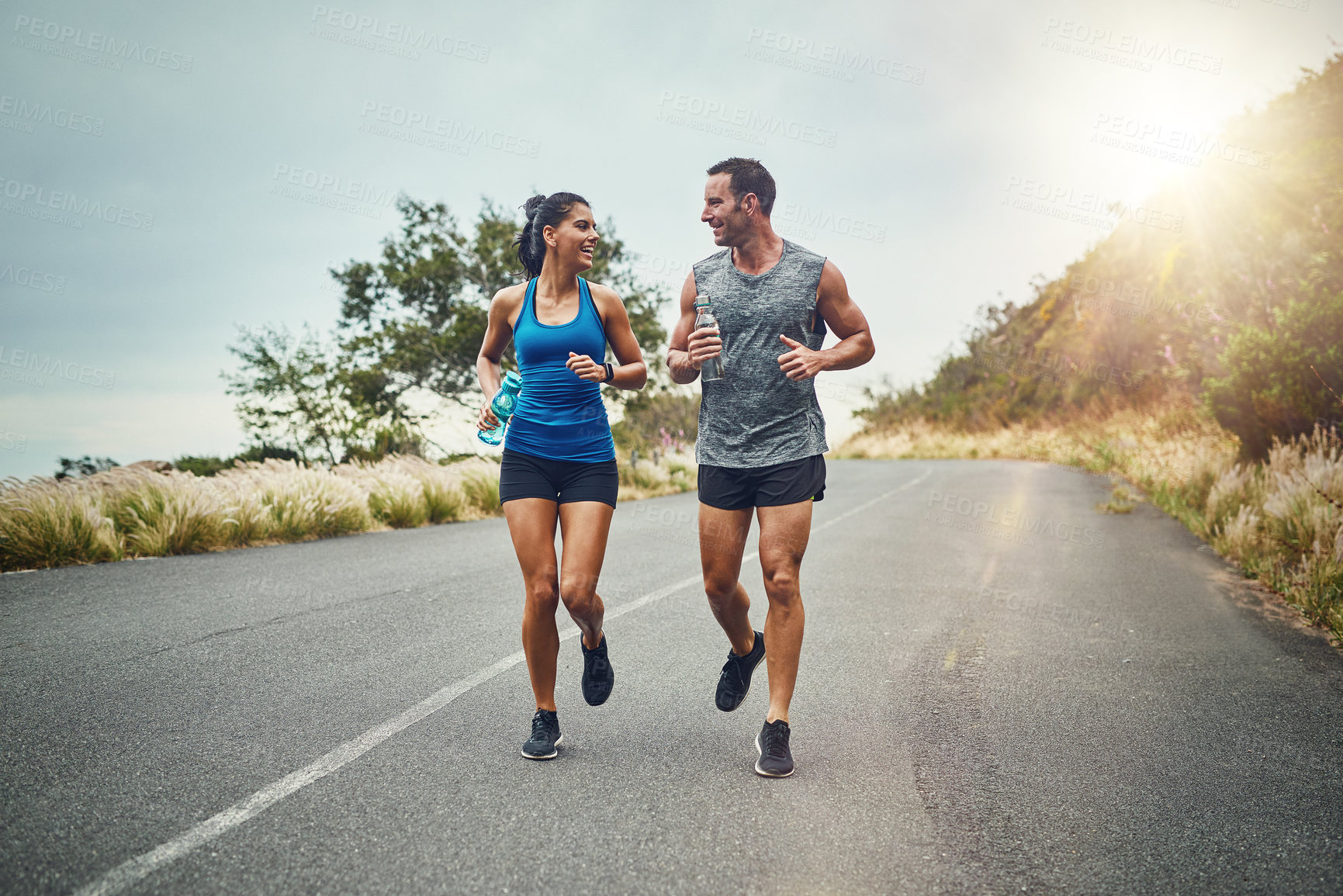 Buy stock photo Couple, road and happy with running for fitness or training, support and love in California. Workout, exercise and people with jogging for health or wellness and wellbeing in morning with lens flare