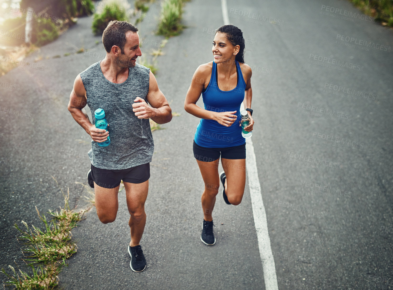 Buy stock photo Fitness, running and couple with smile, race and bottle for hydration with water and outdoor. Road, exercise and people in morning, sportswear and training together, energy and workout in routine