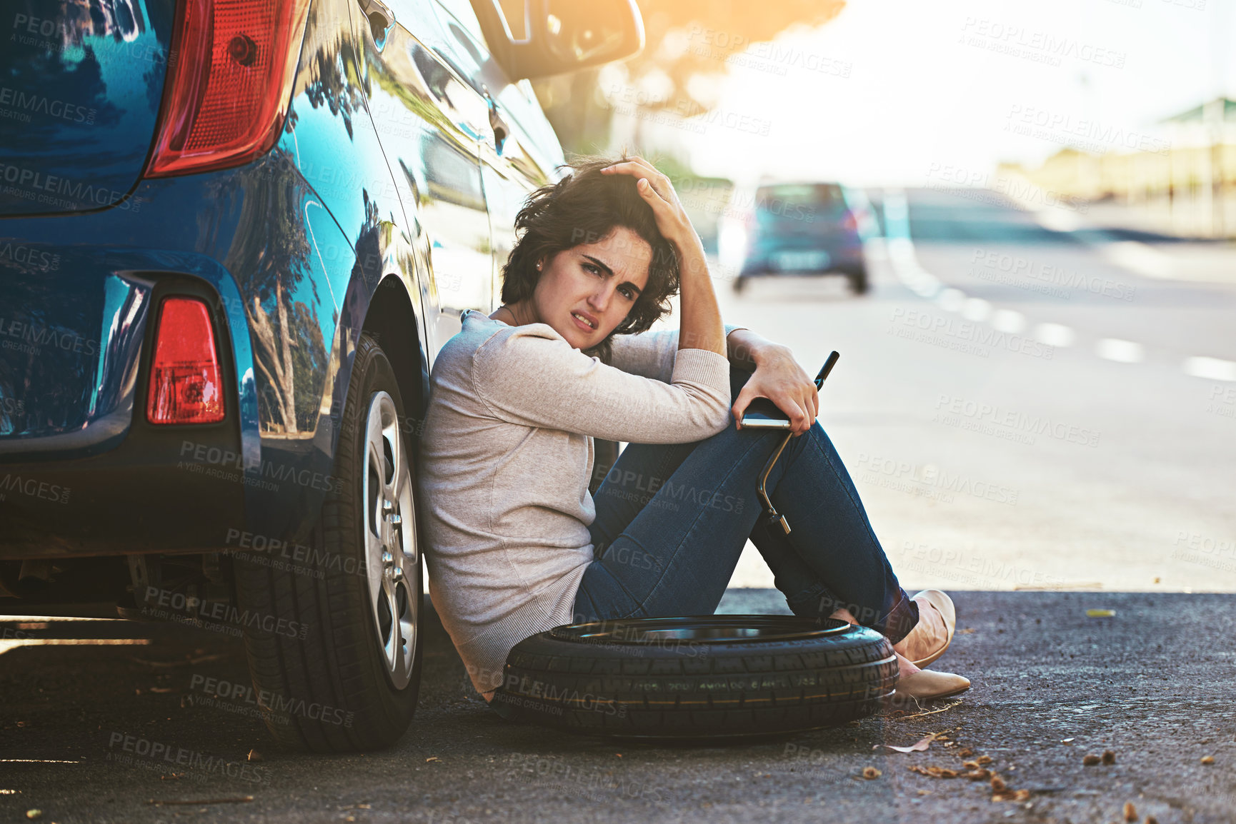 Buy stock photo Shot of a young woman sitting next her broken down car at the side of the road