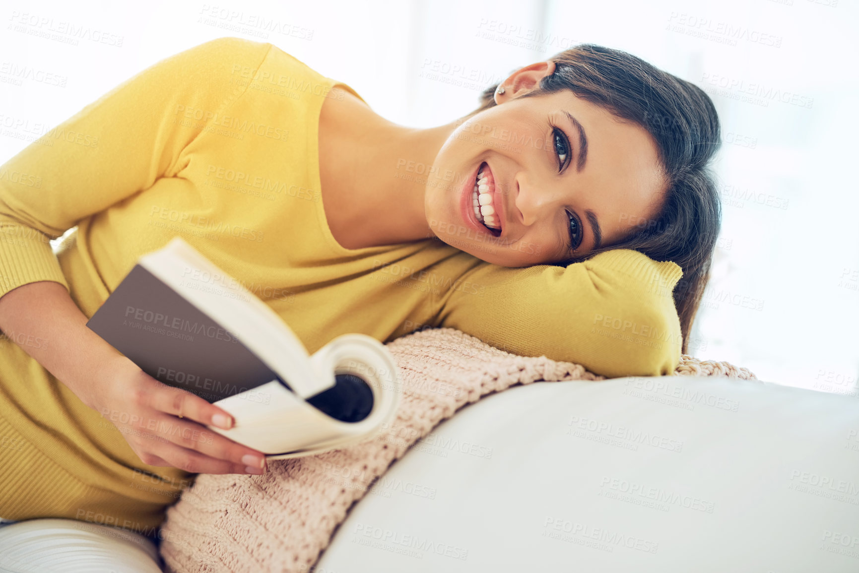 Buy stock photo Shot of a young woman reading a book while relaxing at home
